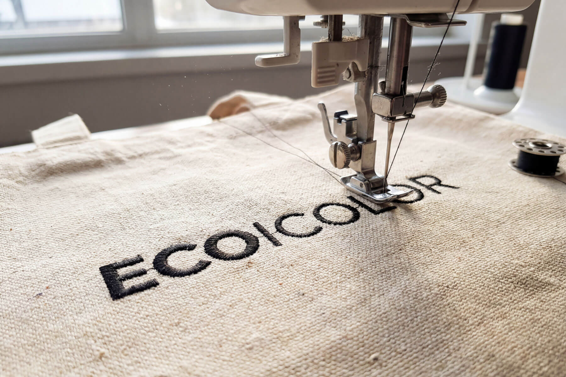 Embroidery machine applying custom brand logo onto organic cotton tote bag